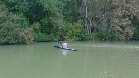 Young woman rowing kayak on river on bank of which there are trees Video stock 124972453