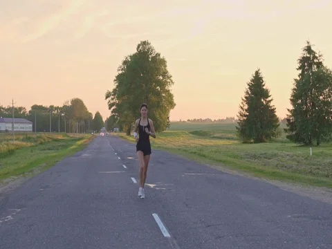 Young woman runner is running down the road in a sporty uniform Stock Footage 77629382