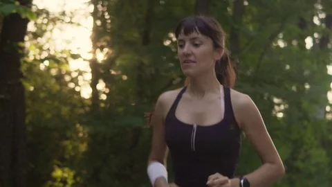 Young woman runner is running down the road in a sporty uniform at sunset Stock Footage 77698342