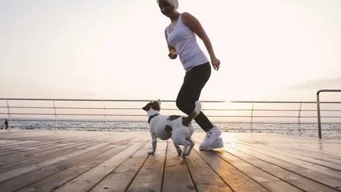 Young woman running with cute dog Jack Russel near the sea, slow motion Stock Footage