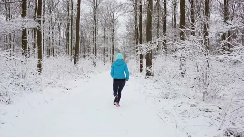 Young woman running down a path in the winter woods through snow Stock Footage 146097573