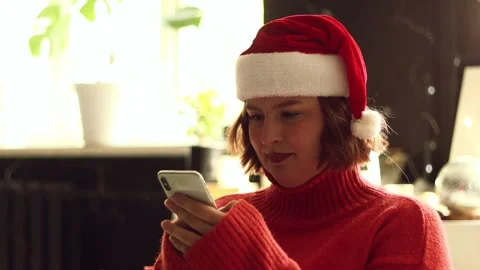 Young woman in Santa hat using smartphone indoors during winter holidays Stock Footage 339079003