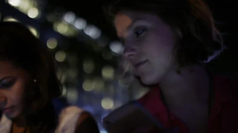 Young woman sat next to her friend as she uses her phone at night in the city Stock Footage