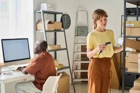 Young woman with scanner checking codes on packed cardboard boxes Photos