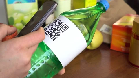 Young woman scanning a QR code on sweet water packaging using smartphone app Stock Footage 132380318
