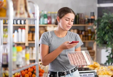 Young woman scanning qr code of raw sausages Foto stock