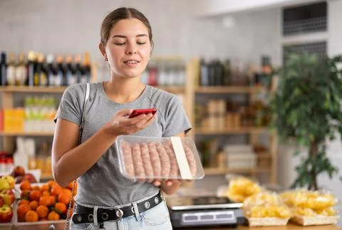Young woman scanning qr code of raw sausages Foto stock