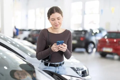 Young woman scanning QR code while choosing car at dealership 스톡 사진