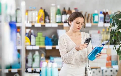 Young woman scanning QR-code on cleaning spray in supermarket Stock Photos