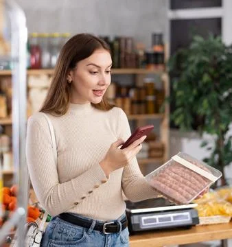 Young woman scanning qr code of raw sausages Stock Photos