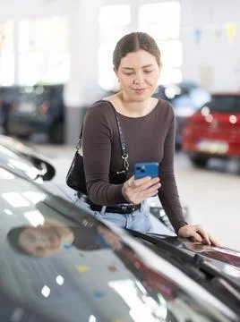 Young woman scanning QR code while choosing car at dealership Fotos de archivo