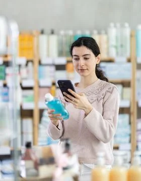 Young woman scanning qr code of mouthwash Fotos de archivo