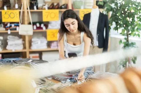Young woman scans QR code and label of trousers or pants using mobile phone Photos