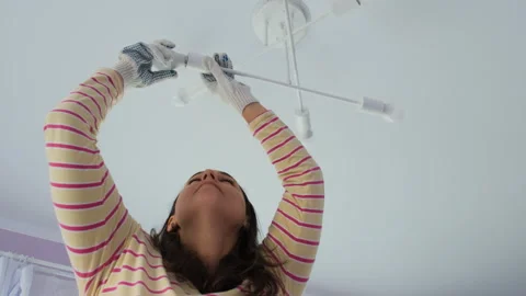 Young woman screwing bulb into ceiling fixture Vídeo Stock 317322053
