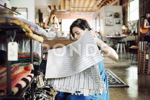 Young woman in a shop, holding a striped tablecloth. Stock Photos