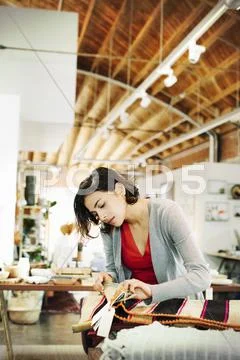Young woman in a shop, looking at small striped rugs. Stock Photos