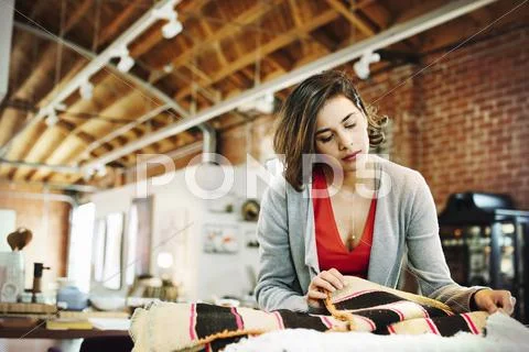 Young woman in a shop, looking at small striped rugs. Stock Photos