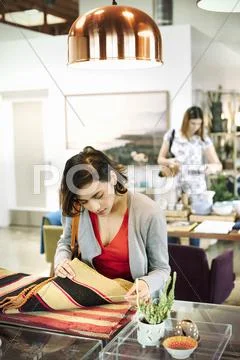 Young woman in a shop, looking at small striped rugs. Stock Photos