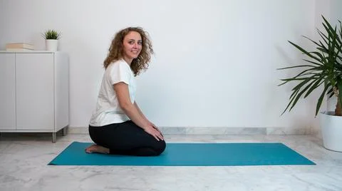 Young woman similing and practicing yoga postures on a blue mat at home. Stock Photos