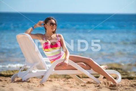 The young woman sit on the sunbed on the sea background Stock Photos