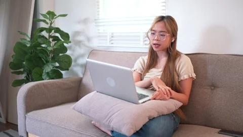 A young woman sits on a couch, using a laptop. She looks engaged in her wor.. Stock Footage 288732020