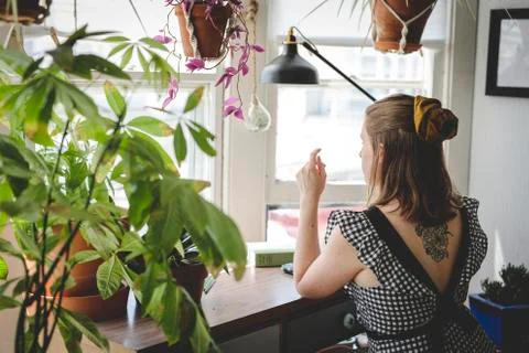 Young woman sits at desk with plants and books Stock Photos