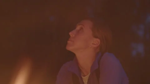 Young woman sits in front of the bonfire burning in the wild Stock Footage 341663453