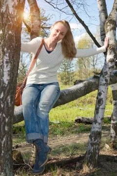 Young woman sits on a trunk of the tumbled down birch.. Stock Photos