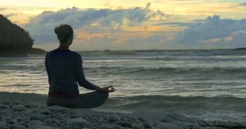 Young woman sits in yoga position meditating by the ocean Stock Footage 59136436