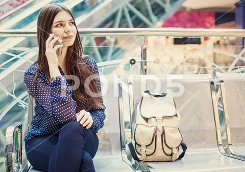 Young woman is sitting at an airport and speaking by her phone. Stock Photos