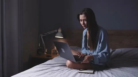 Young woman sitting on bed and working from home using laptop Stock Footage