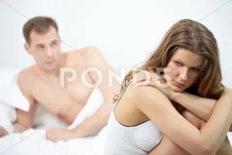 A young woman sitting on bed distressed against her lying husband Stock Photos