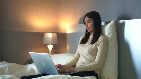 Young woman sitting on bed using laptop for work in bedroom at home. Stock Footage 233278366