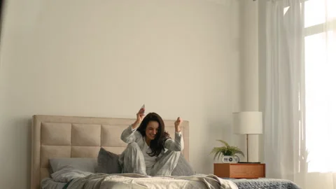 Young woman sitting on bed using mobile phone cellphone notification message Stock Footage 276201563
