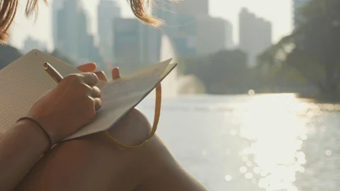 Young woman sitting on the bench in park and writing in diary, close-up Stock Footage
