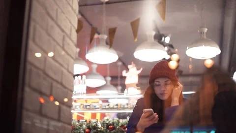 Young woman sitting in cafe using smartphone. New year's decorations Stock Footage 83072983