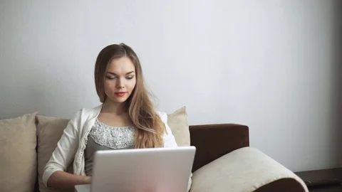 Young woman sitting on couch using laptop and smiling Stock Footage 74434960