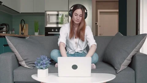 Young woman sitting on couch using laptop and concentrates on work Stock Footage 169620309