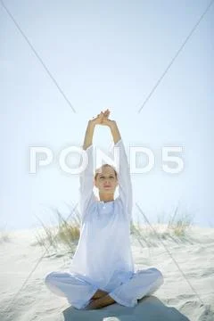 Young Woman Sitting On Dune, Stretching Arms Over Head