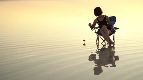 Young woman sitting on fisherman chair and reading book, drinking wine, enjoying Stock Footage