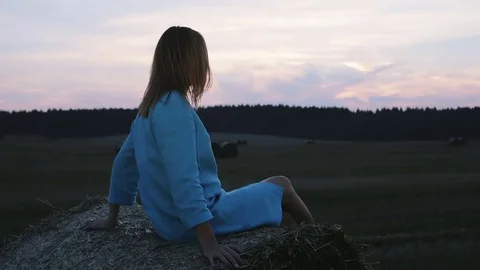 Young woman sitting on a haystack during sunset. Stock Footage 69945954