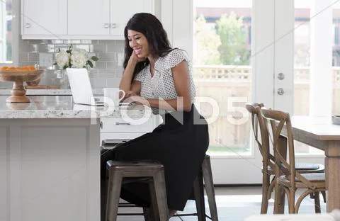 Young Woman, Sitting At Kitchen Counter With Coffee And Laptop