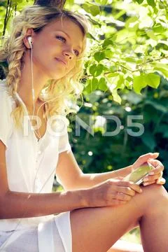 Young woman sitting near the tree and listening to music Stock Photos