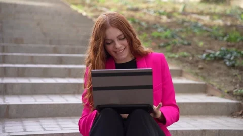 A Young Woman Sitting Outside, Using Her Laptop While Dressed in a Bright Pink Stock Footage 311248757