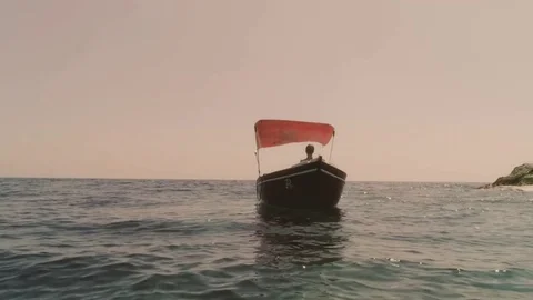 Young woman sitting on a red boat in the middle of the ocean stretches her arms Stock Footage