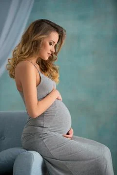 Young woman sitting on the sofa. Pregnant blonde, pending, parenthood concept Stock Photos