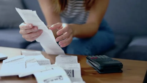 Young woman sitting on sofa using calculator to calculate household expenses Stock Footage 243208723