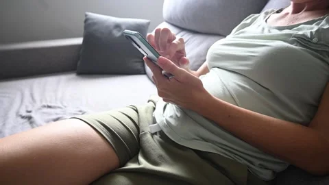 Young woman sitting on a sofa using her smartphone at home Stock Footage 320239686