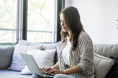 Young woman sitting on a sofa using a laptop at home, focused on online sho.. Stockfoto's