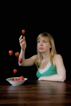 Young woman sitting at table and reaching for strawberry floating mid-air Stock Photos